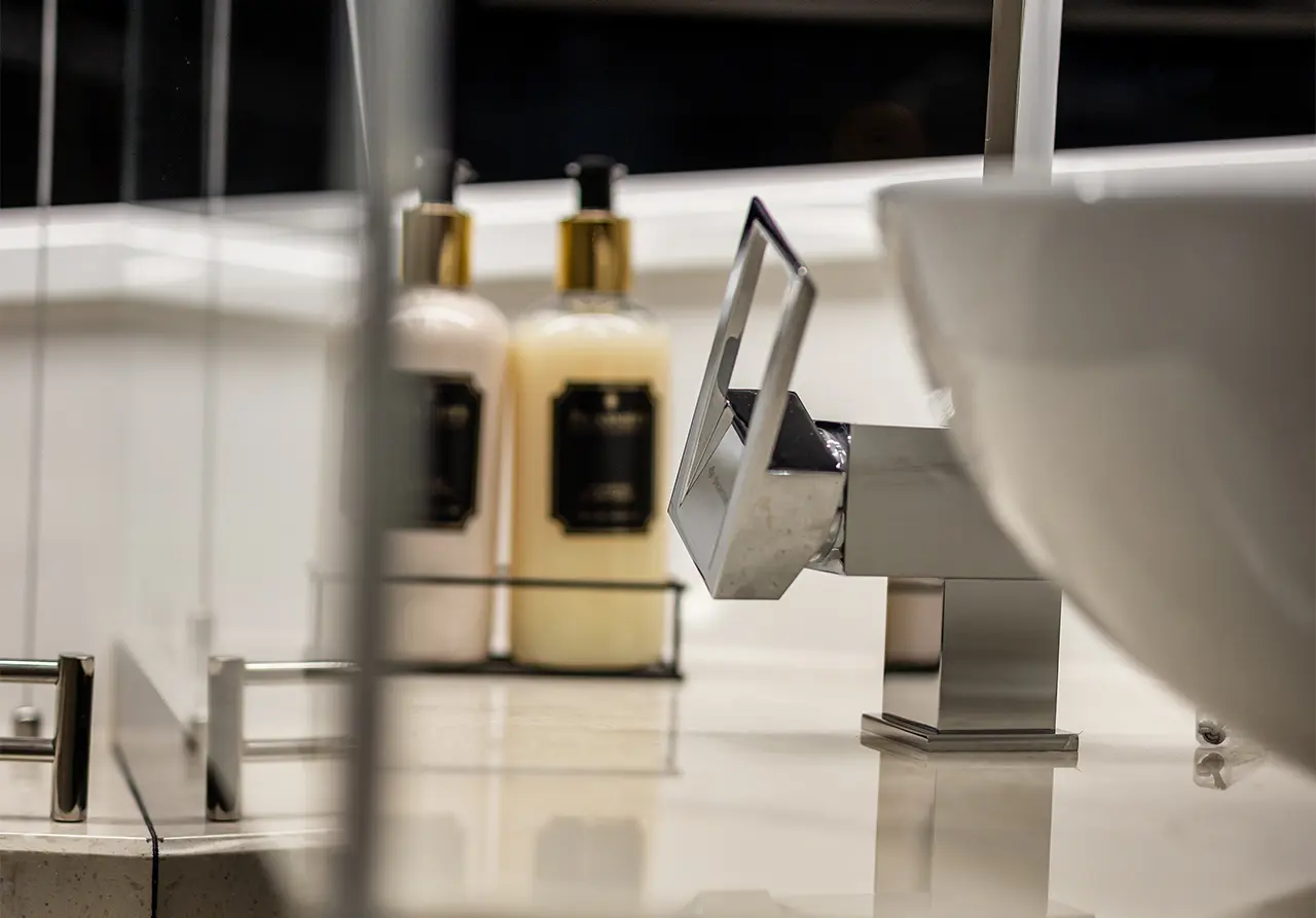 Modern bathroom setting featuring a sleek silver tap, white basin, and two bottles of toiletries with black labels.