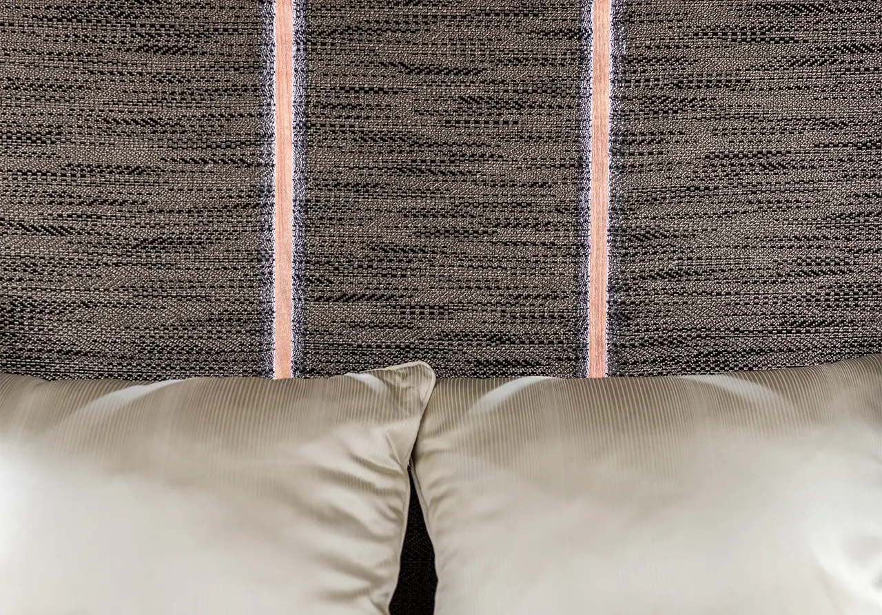 Textured fabric headboard with two cream cushions resting below, featuring subtle line patterns. Ideal for bedroom decor.