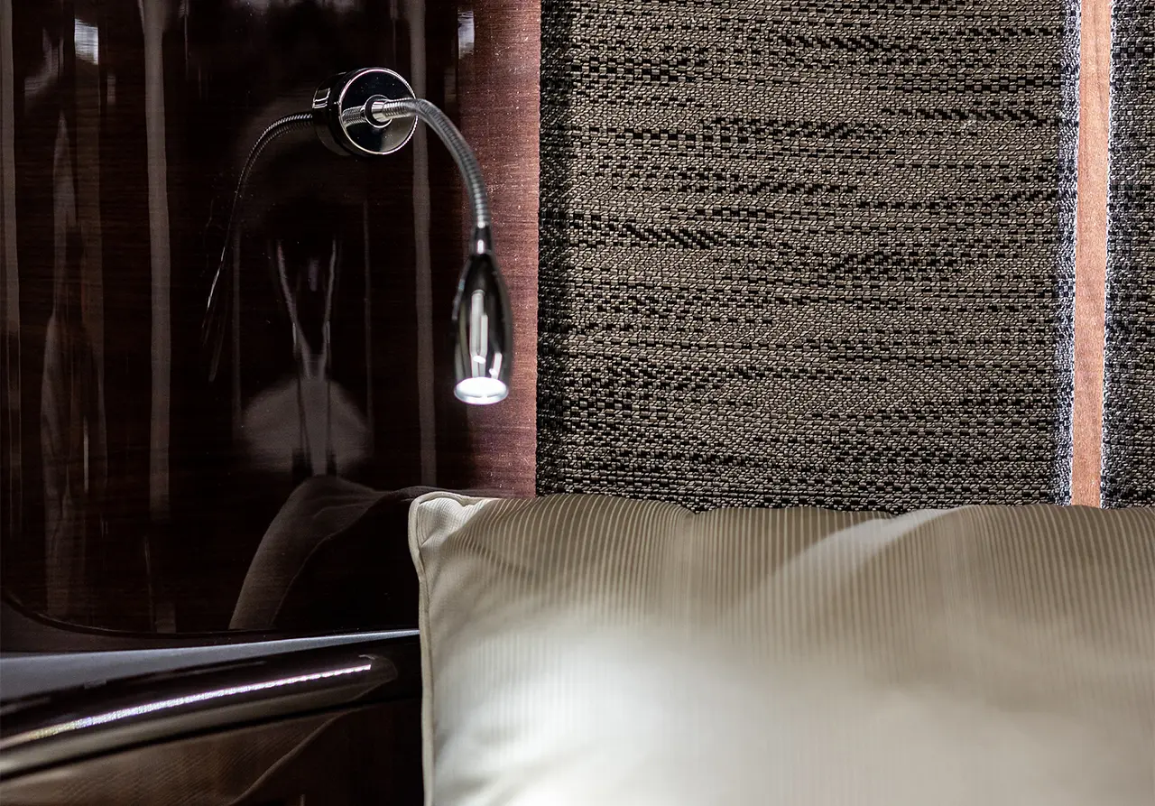 Modern bedside area featuring a sleek reading light and a striped pillow against textured fabric wall.