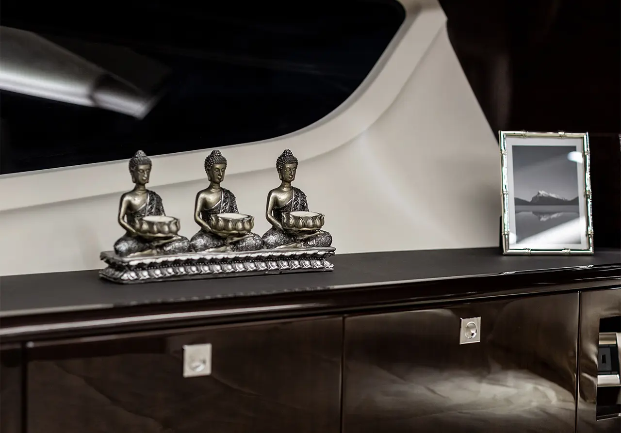 Three silver Buddha figurines with bowls on a dark wooden surface, next to a framed black and white mountain photo.