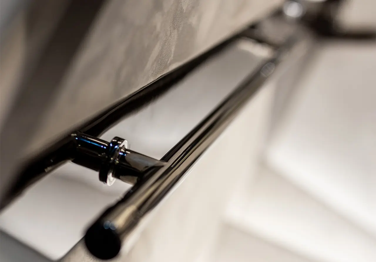 Close-up of a sleek chrome towel rail against a textured wall, reflecting soft light in a modern bathroom setting.
