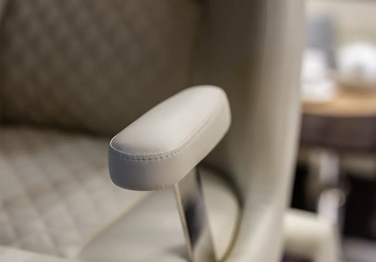 Close-up of a white, padded armrest on a stylish chair, featuring sleek metal support and quilted background.