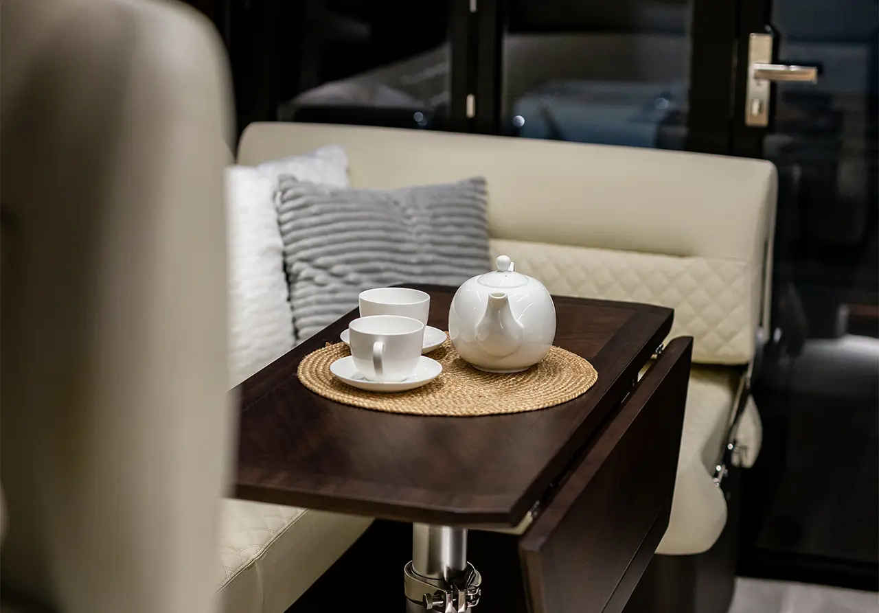 A cosy seating area featuring a wooden table with a tea set, two cups, and a teapot on a woven placemat.
