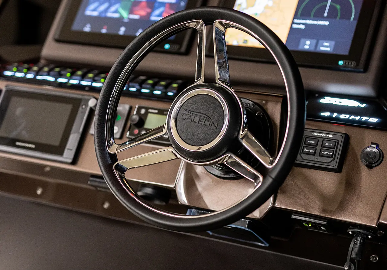 Steering wheel with 'Galeon' branding in a yacht control panel, featuring digital displays and navigation controls.