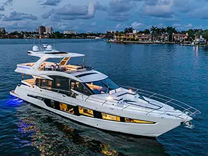 Luxury white yacht sailing on calm water, featuring modern design and illuminated interior, with a city skyline in the background.