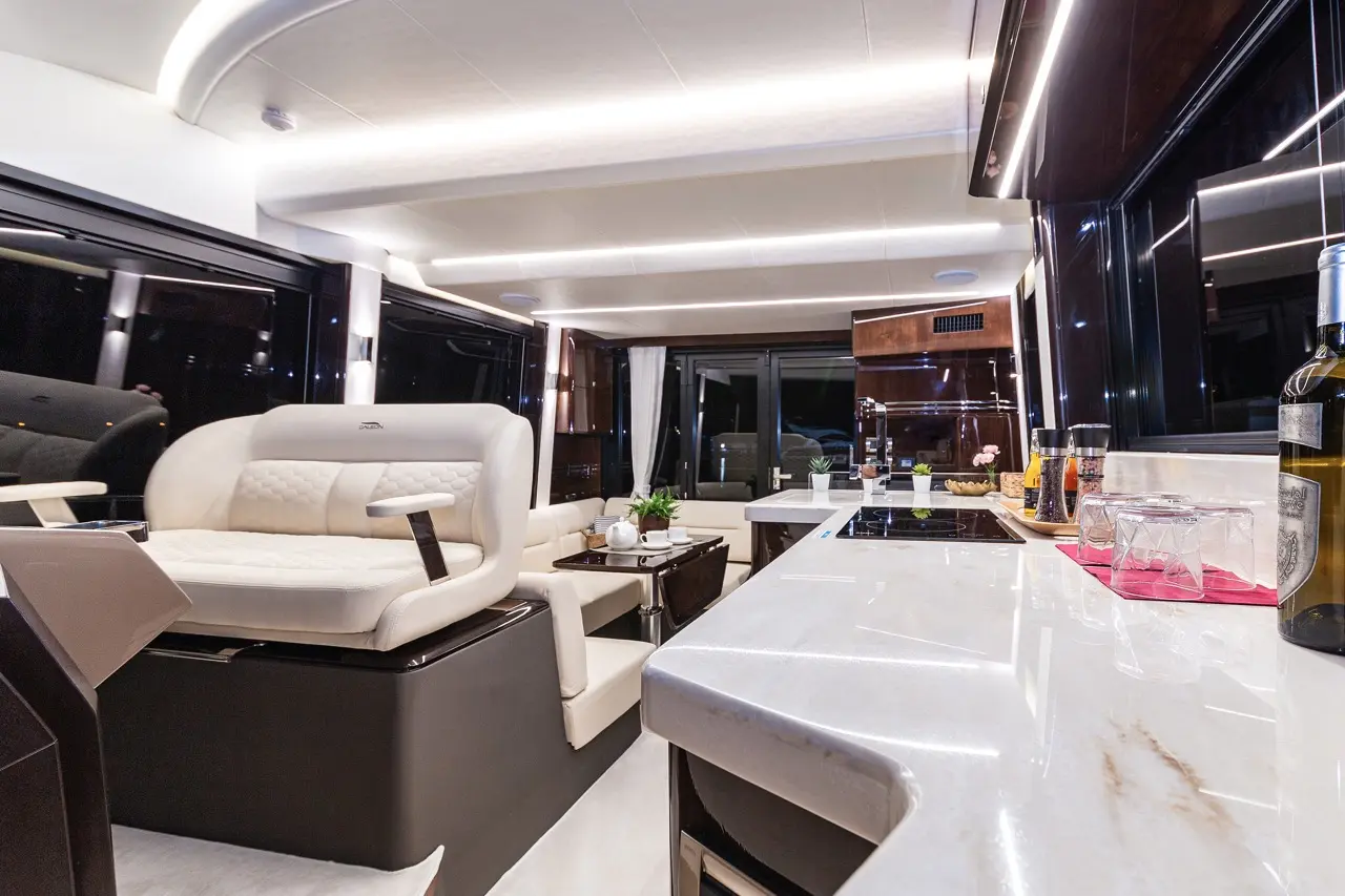 Modern yacht interior showcasing a spacious lounge with a white sofa, stylish kitchen, and ambient lighting.