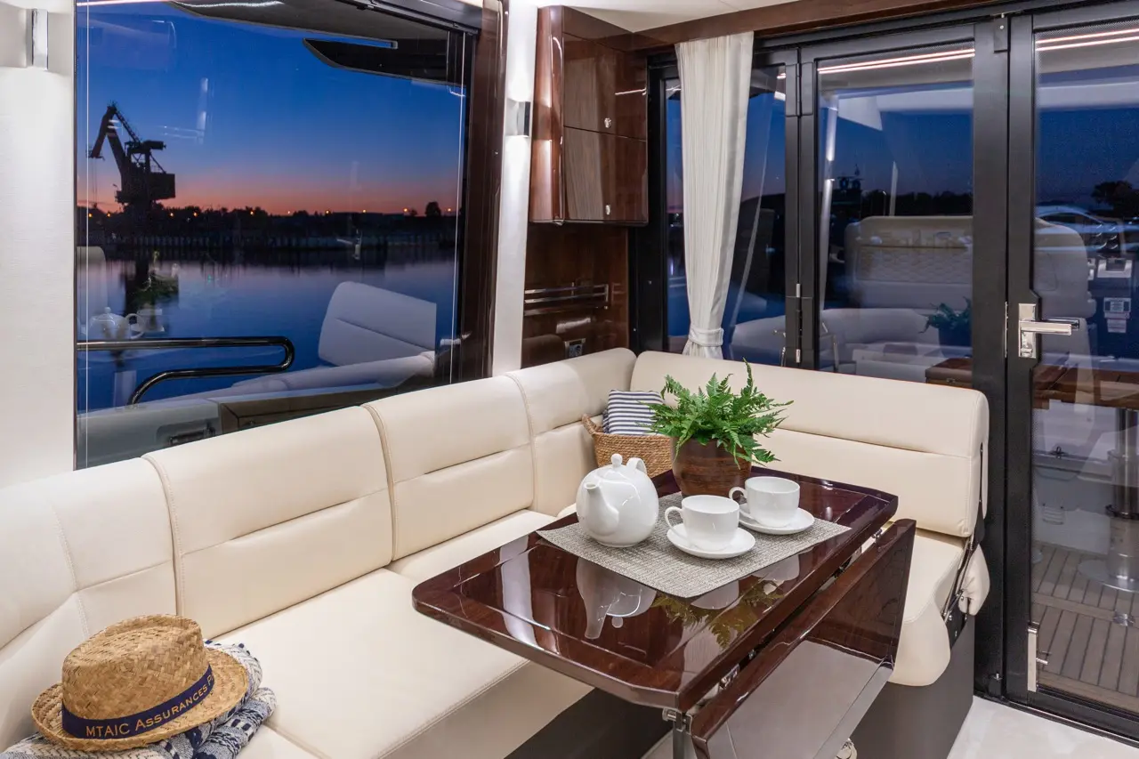 Luxury yacht interior featuring a stylish lounge, sunset view, tea set, and decorative plant on a polished table.