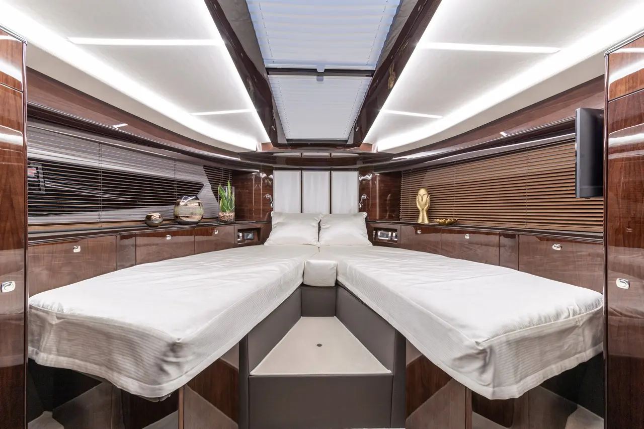 Luxurious yacht cabin featuring twin beds with neutral linens, polished wood finishes, and decorative elements like a plant and sculpture.