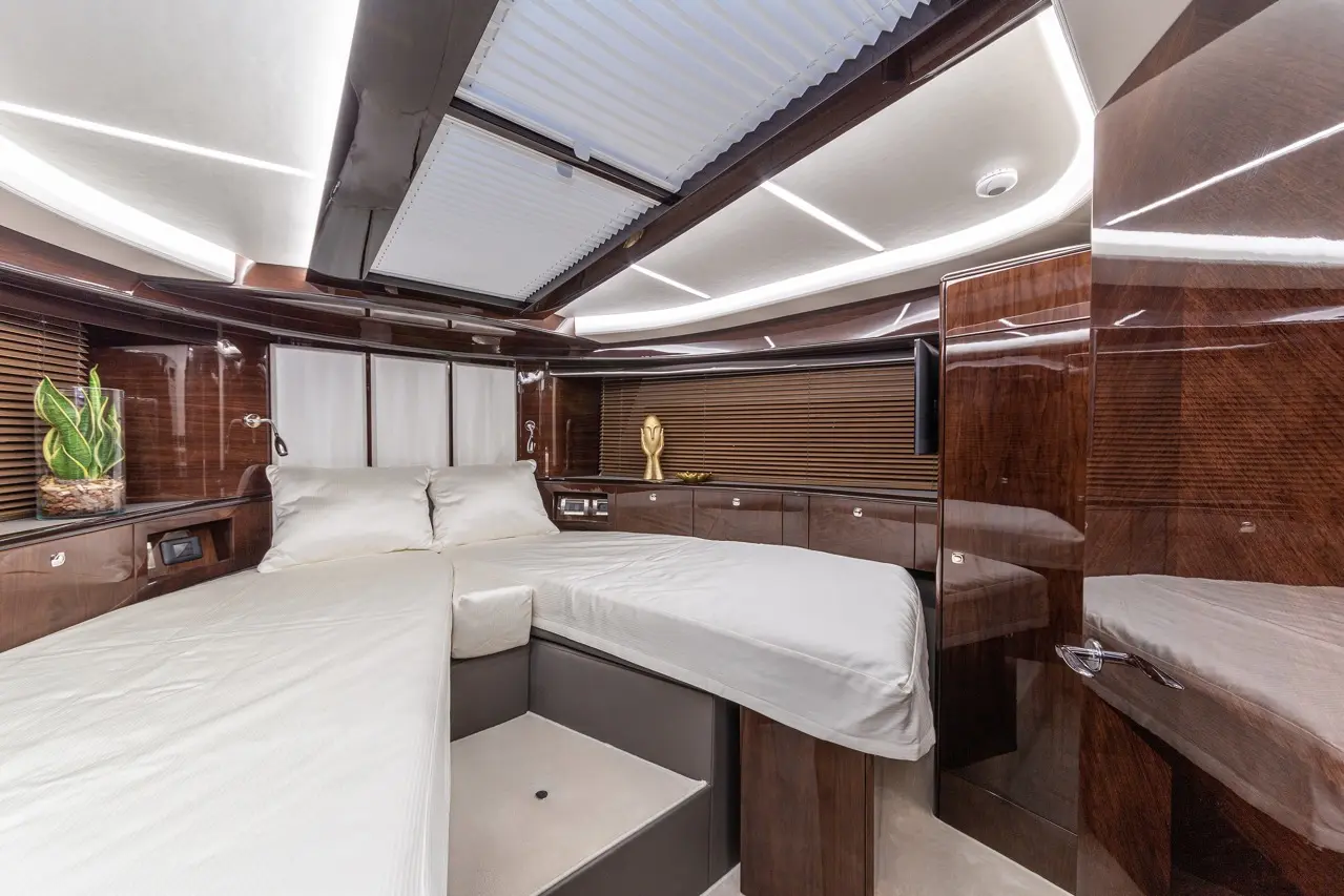 Luxury yacht interior featuring two beds, elegant wood finishes, decorative plant, and modern lighting above.