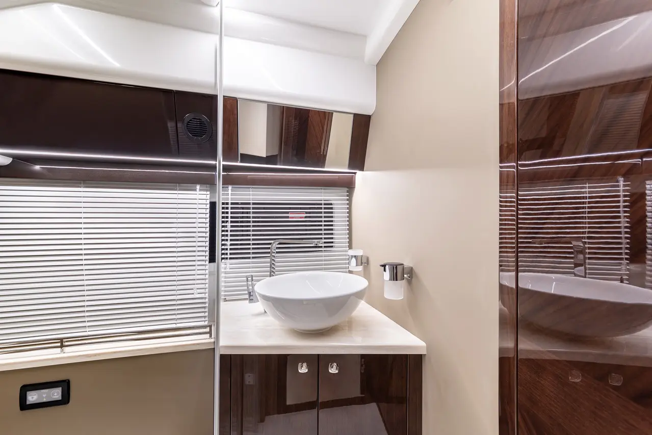 Modern bathroom featuring a white basin on a marble vanity, mirrors, and wooden cabinetry with blinds in the background.
