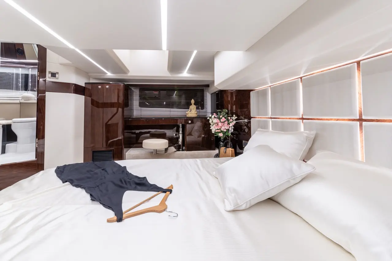 Luxurious bedroom with a white bed, decorative pillows, a black dress on a wooden hanger, and a flower arrangement in the background.