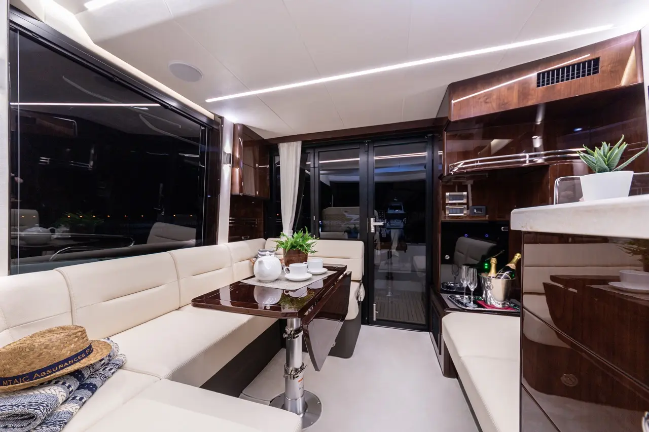 Luxurious yacht interior with a modern dining area, glass doors, potted plants, and a table set with cups and champagne.
