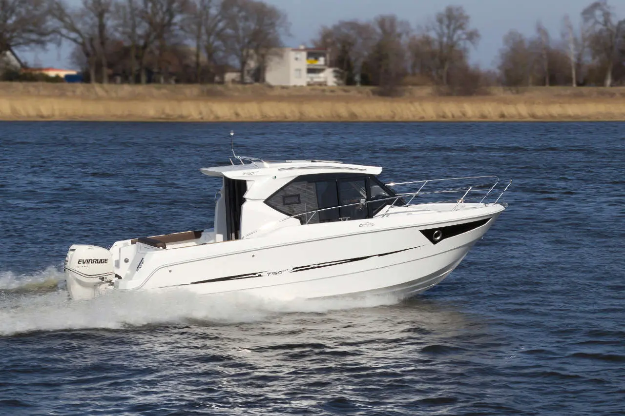 A white motorboat glides across calm water, with trees and buildings in the background, showcasing leisure and boating activities.