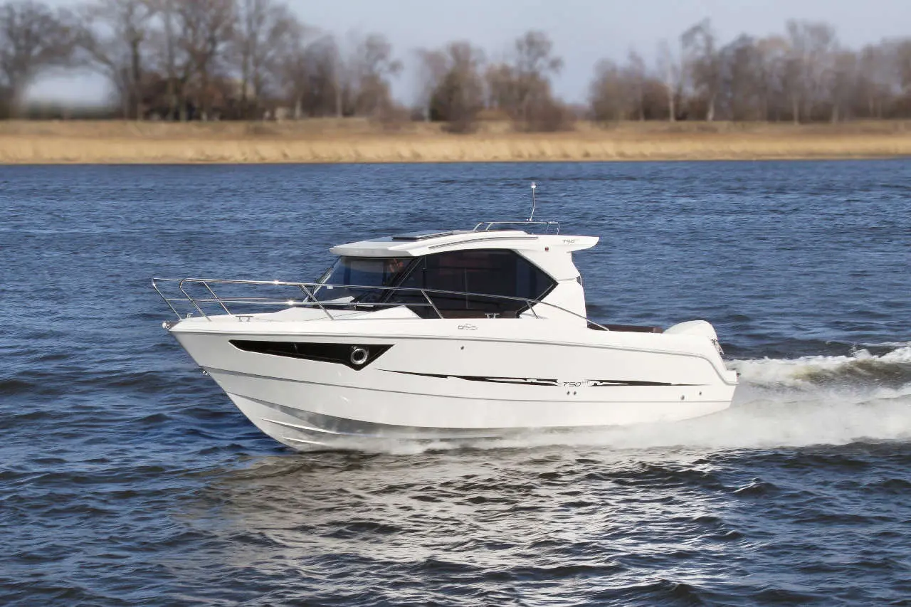 A sleek white motorboat glides through the water, with a blurred riverbank and trees in the background.