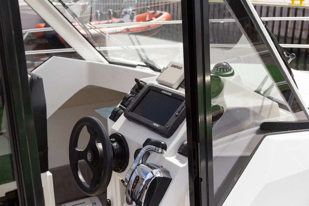 Boat dashboard featuring a steering wheel, Lowrance display, and compass, with a red rescue boat visible in the background.