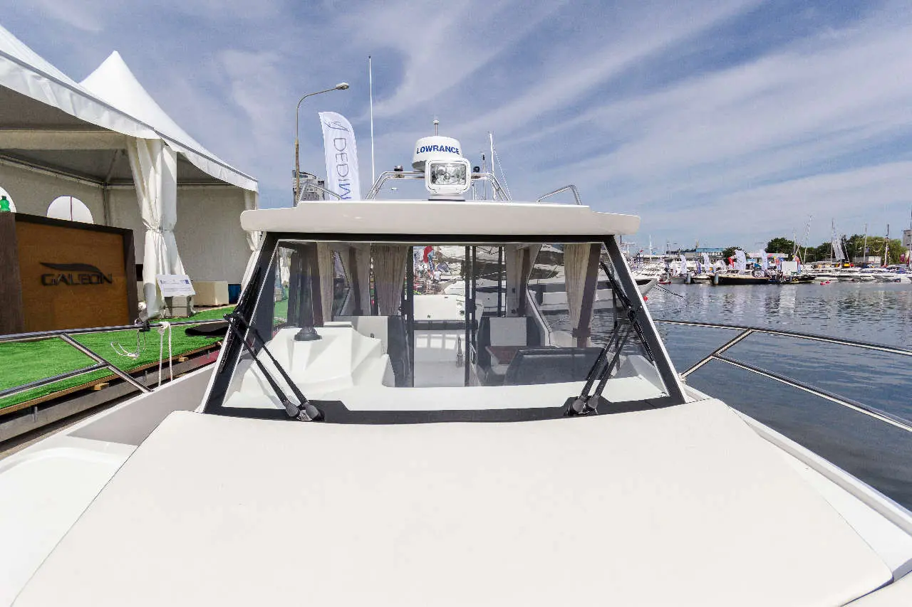 View of a modern motorboat’s cockpit and windshield at a marina, featuring a LOWRANCE equipment and nearby tented exhibits.