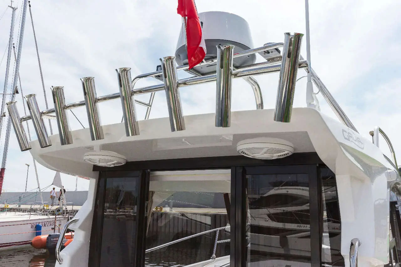 View of a yacht's upper deck featuring polished stainless steel rod holders, a red flag, and large glass windows.