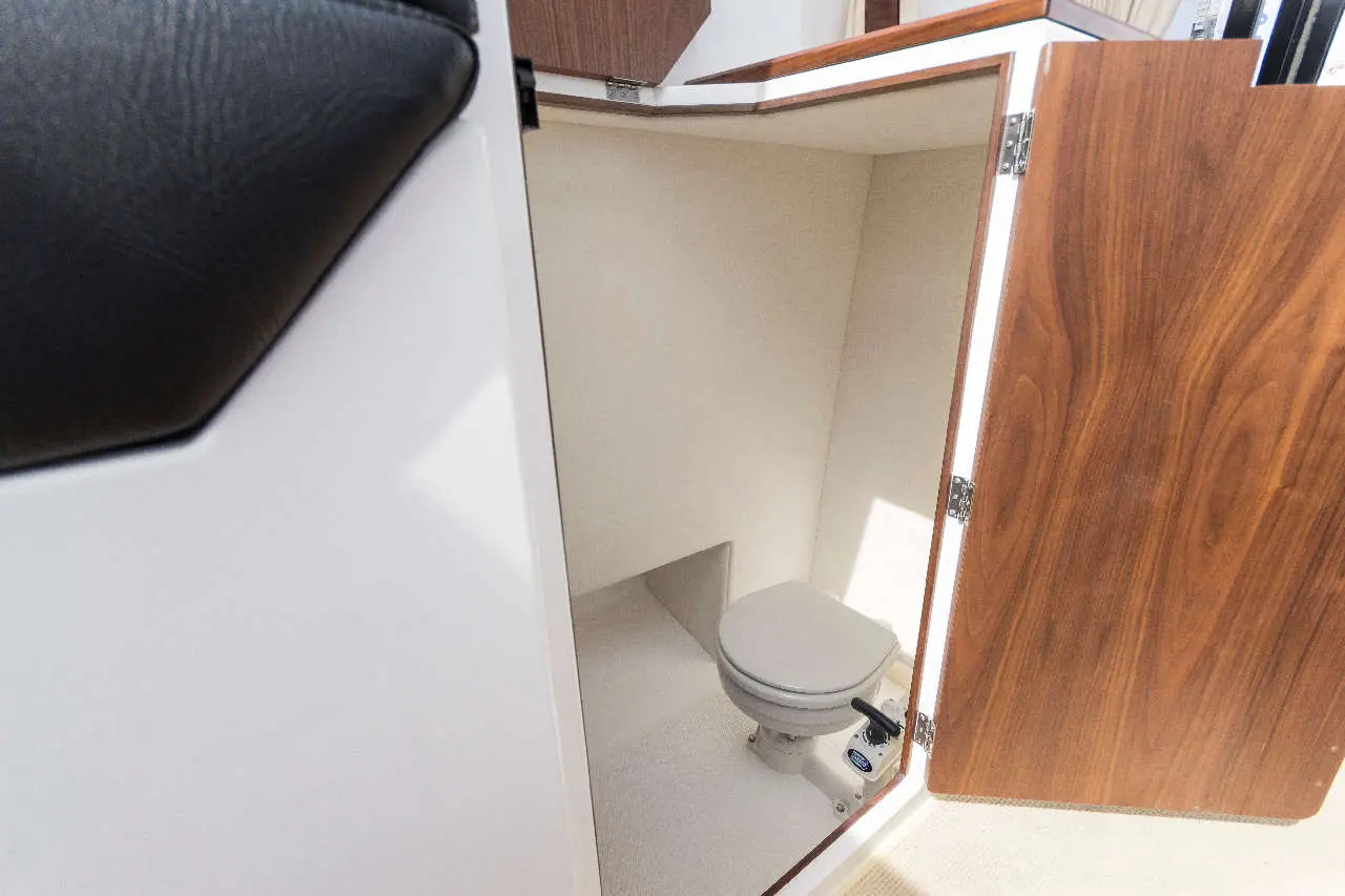Compact boat bathroom featuring a marine toilet, with open wooden doors and a light-coloured interior.