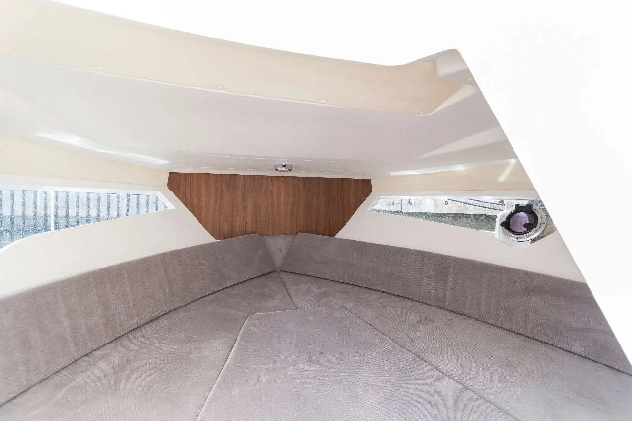 Interior view of a boat featuring a grey cushioned seating area and wooden paneling near the triangular windows.