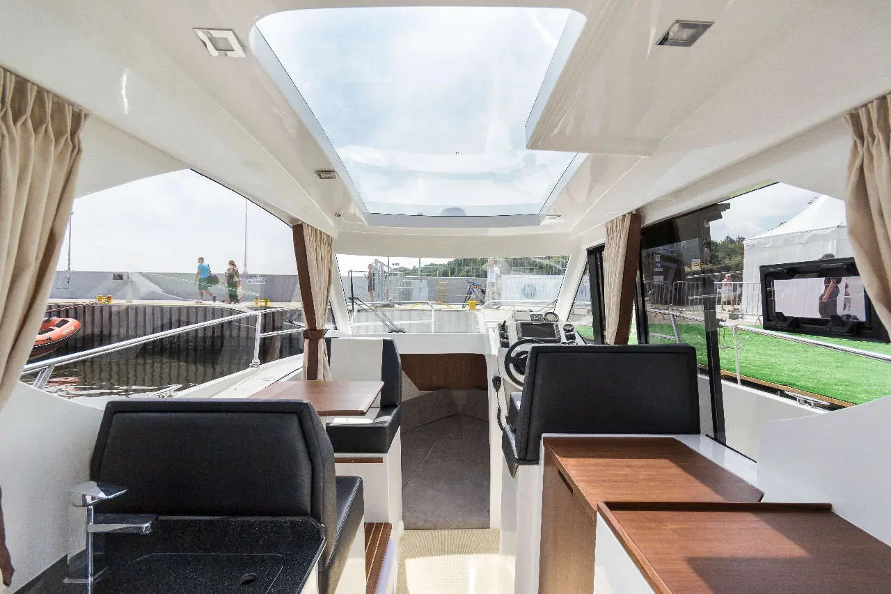 Interior view of a modern boat with a panoramic window, featuring seating areas and a control console.