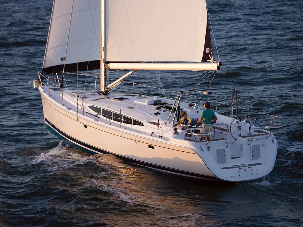 Sailing yacht with two people on deck, navigating through waves under clear skies, showcasing a relaxed boating lifestyle.