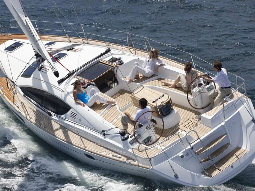 Four people relax and navigate on a sleek sailing yacht, enjoying a sunny day on the water with a dynamic view.