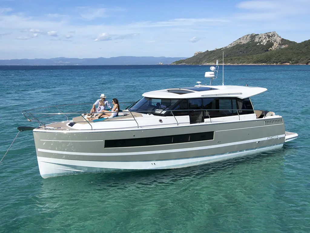 A modern boat, the NC14, floats on clear blue water, with two people relaxing and enjoying a sunny day on board.