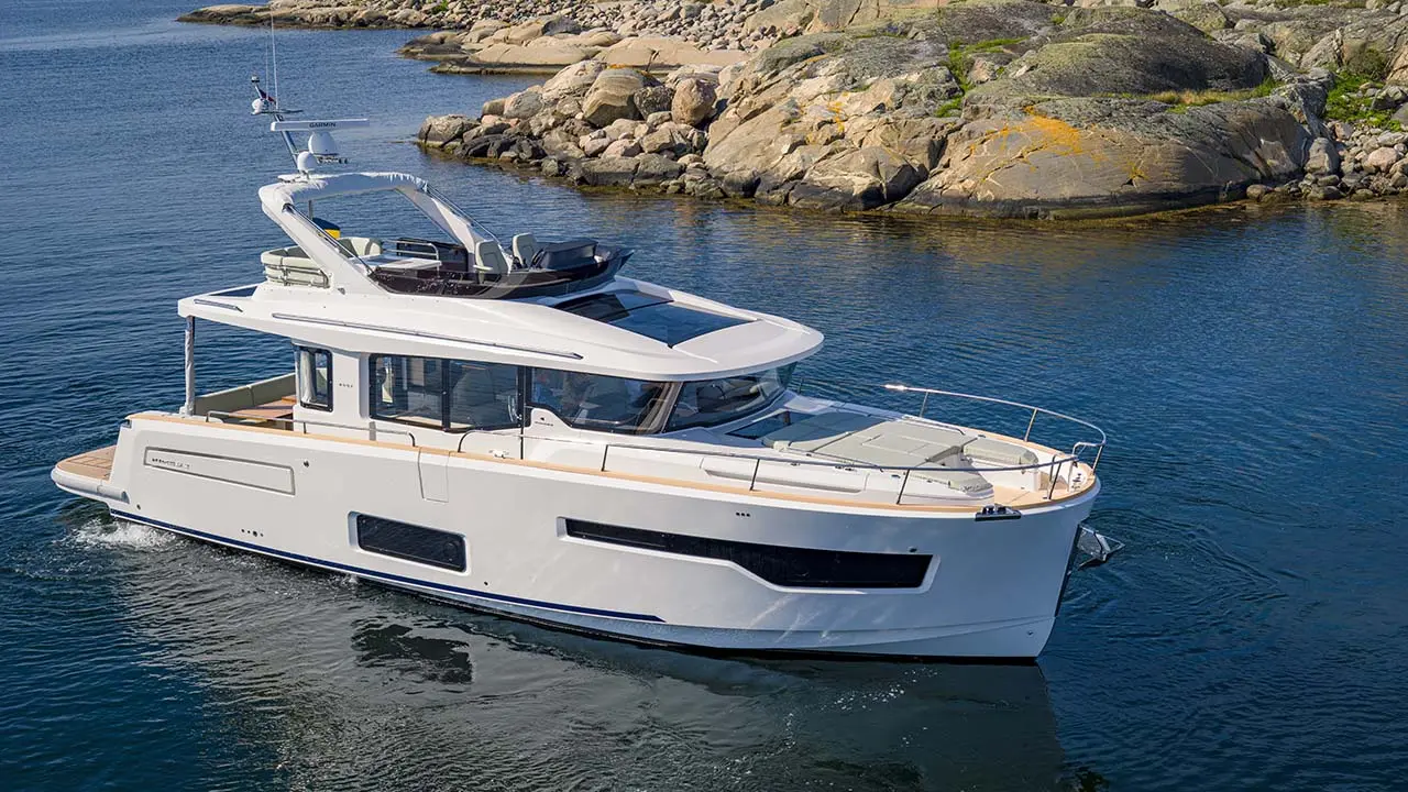 White motor yacht cruising through calm blue water beside a rocky shoreline.