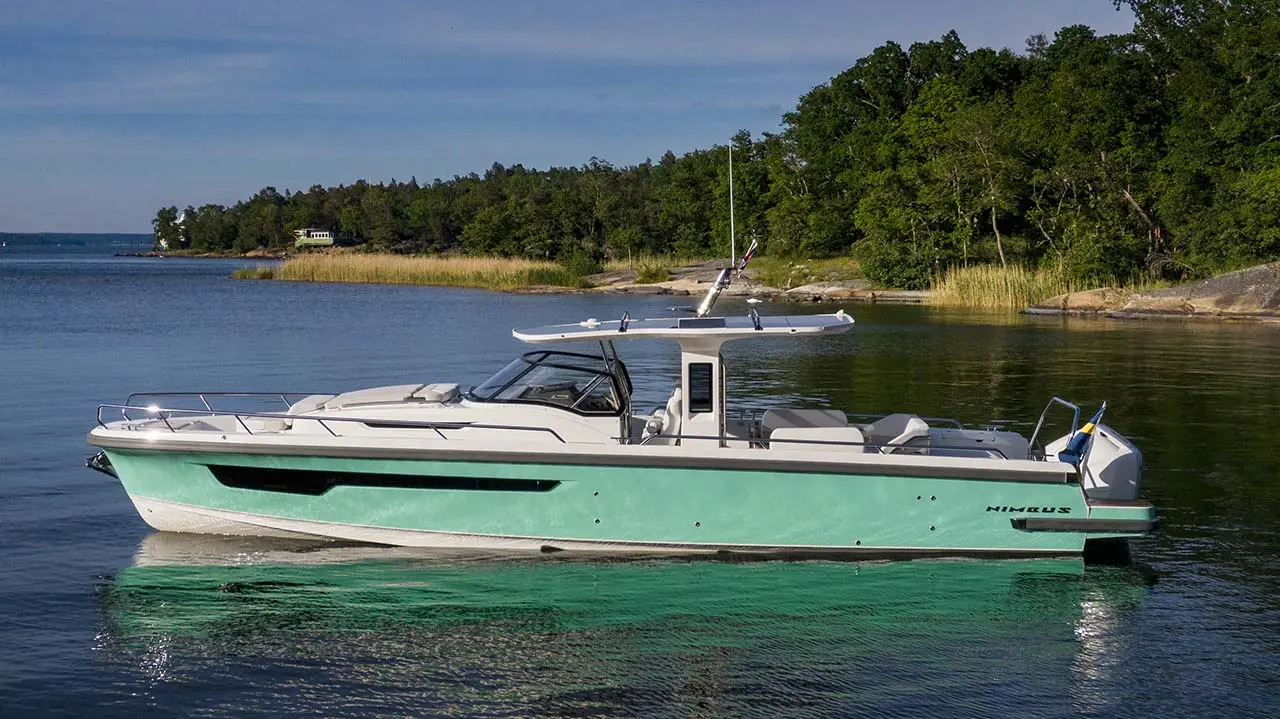Turquoise Axopar motorboat cruising on calm coastal waters beside a wooded shoreline, with Swedish flag visible.
