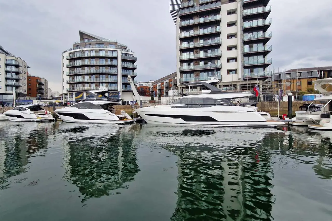 Luxury boats docked at a marina with modern apartment buildings in the background, reflecting in the calm water.