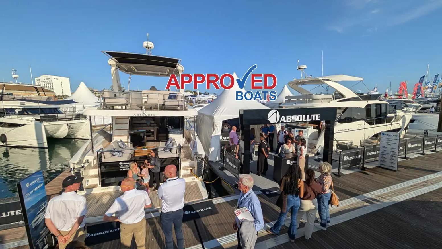 People engage with the Absolute Boats display at a marina, featuring luxury yachts and promotional signage.