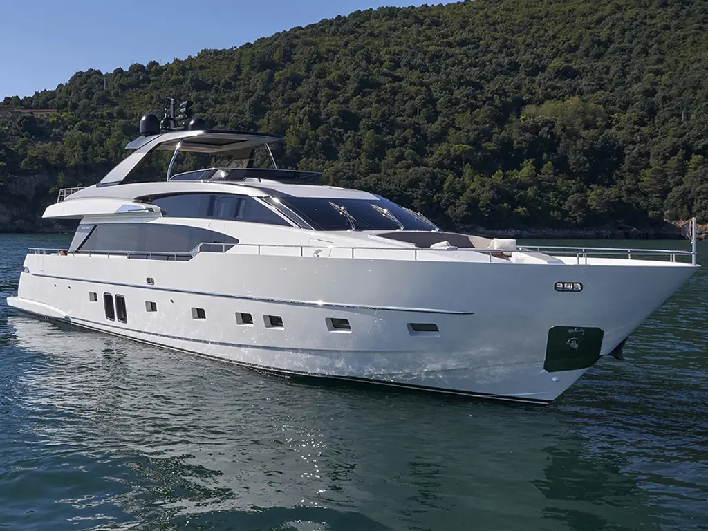 Luxury yacht docked in clear waters, surrounded by lush green hills under a bright blue sky.