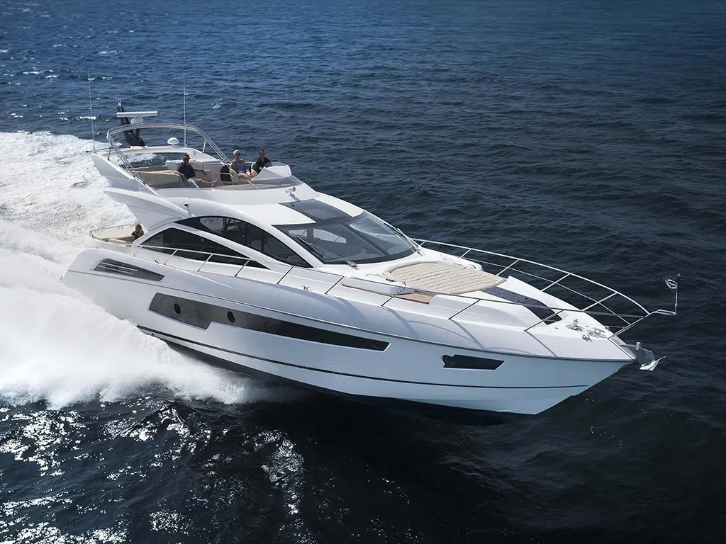 A sleek white luxury yacht speeds through blue ocean waves, with passengers enjoying the sun on deck.