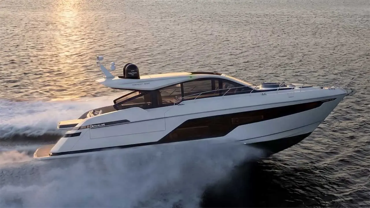 White Fairline motor yacht speeding across the sea, creating a large wake in golden evening light.