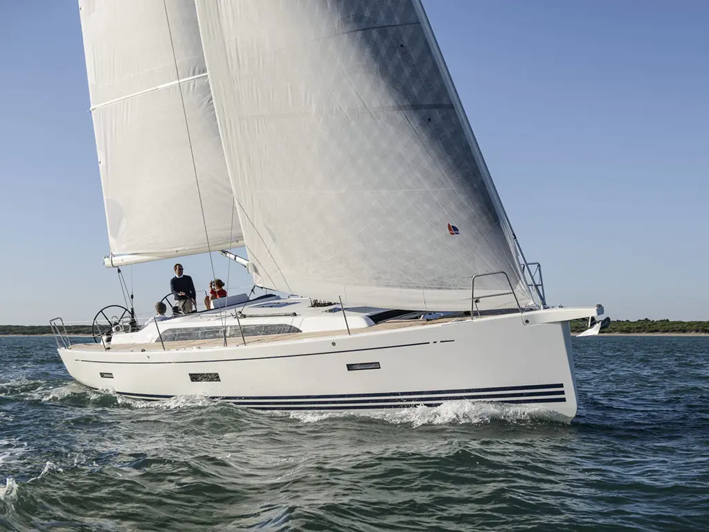 A white sailing yacht with two people on board gliding through blue waters under clear skies and full sails.