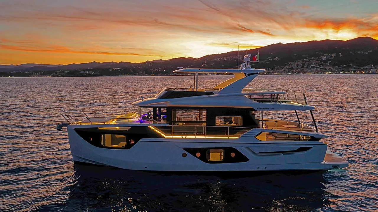 Luxury motor yacht on a lake at sunset, with a mountain coastline and illuminated cabin.