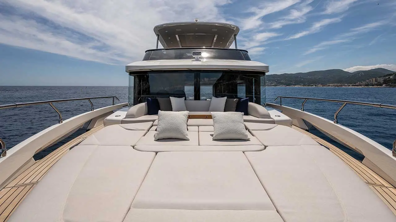 Luxury yacht bow with cream sun loungers and cushions, overlooking the sea and mountainous coastline.