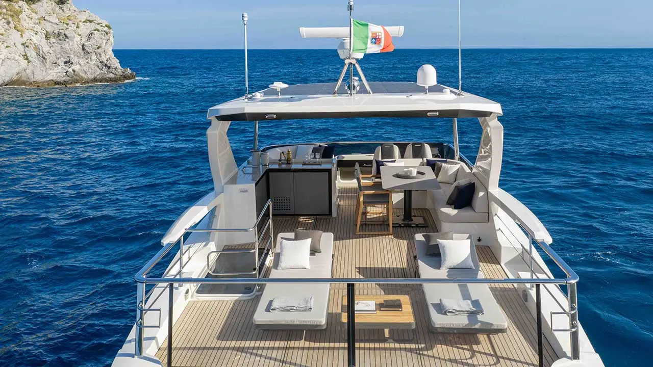 Luxury yacht deck with outdoor seating and Portuguese flag on the Mediterranean Sea beside a rocky coast