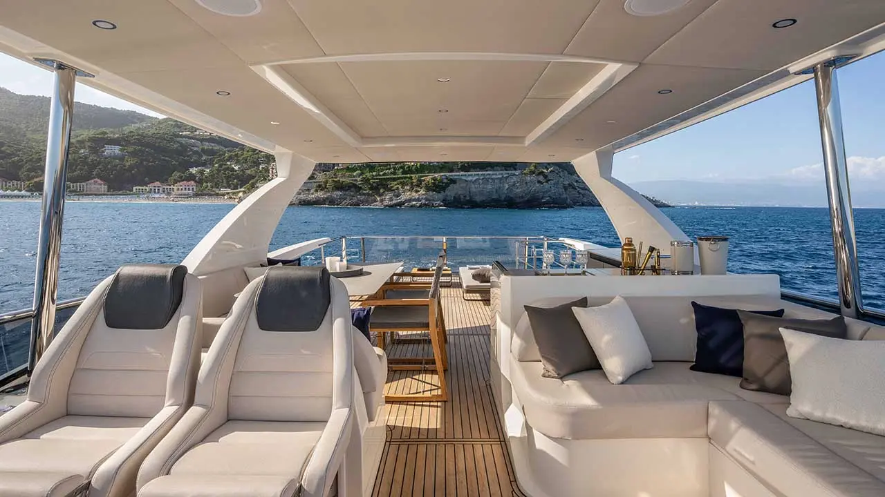Luxury yacht deck with white seating overlooking blue sea and a rocky Mediterranean coastline.