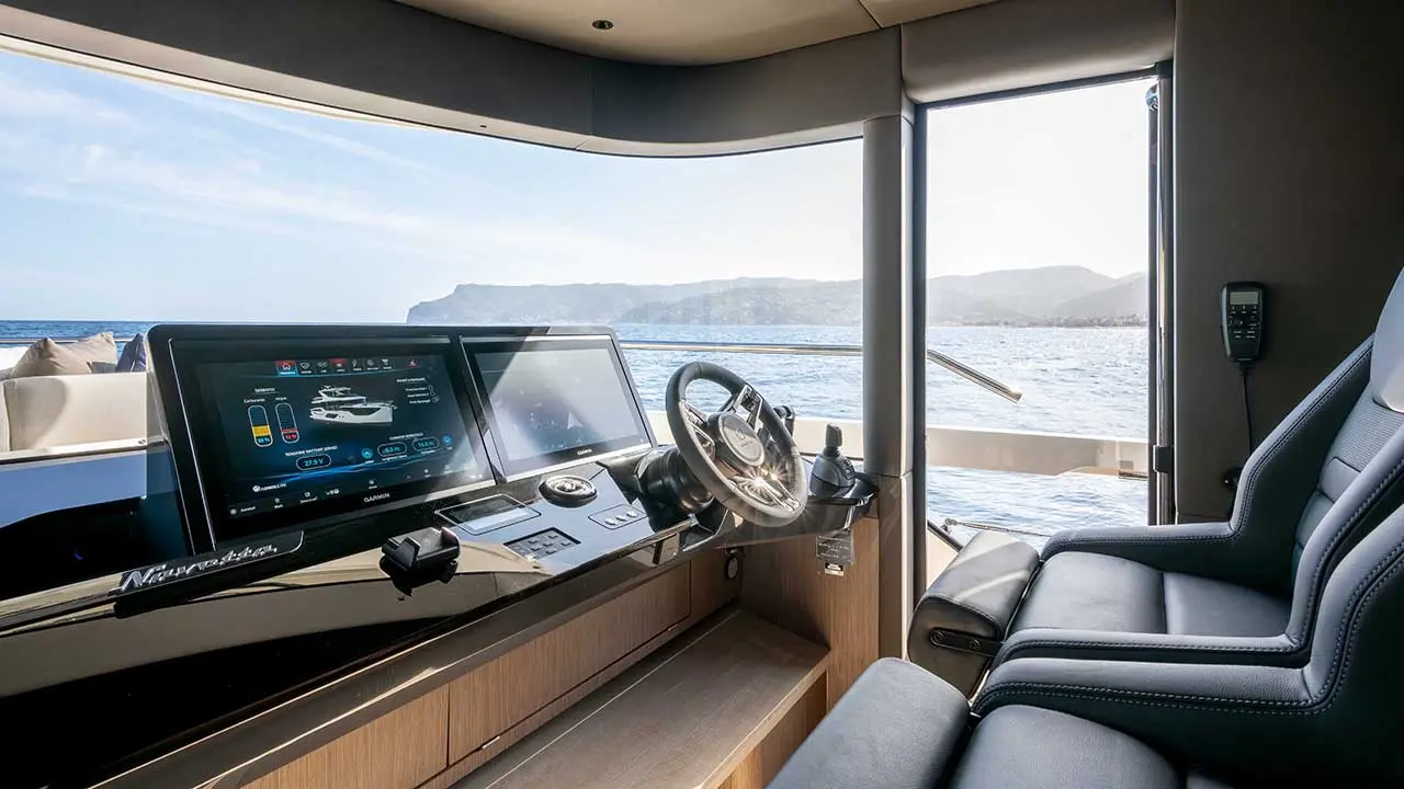 Luxury Navetta yacht helm with Garmin displays and steering wheel, overlooking the sea and rugged coastline.