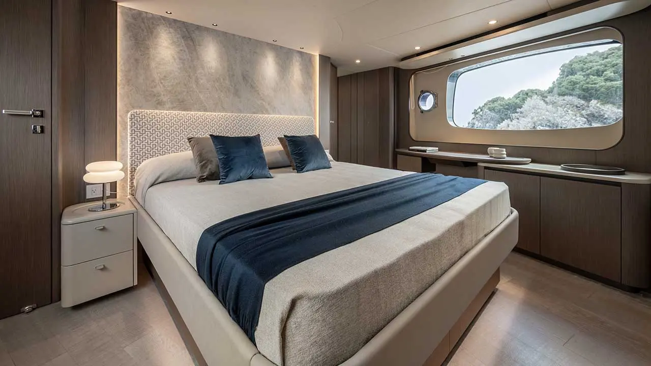 Modern yacht bedroom with a double bed, navy throw, bedside table and panoramic window overlooking green hills.