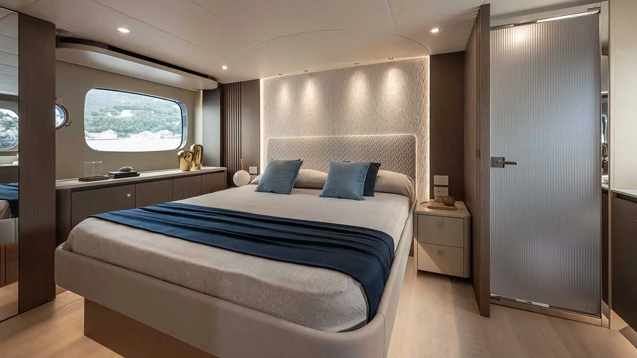Luxury yacht bedroom with a double bed, blue throw, built-in cabinetry, porthole windows and a wardrobe.