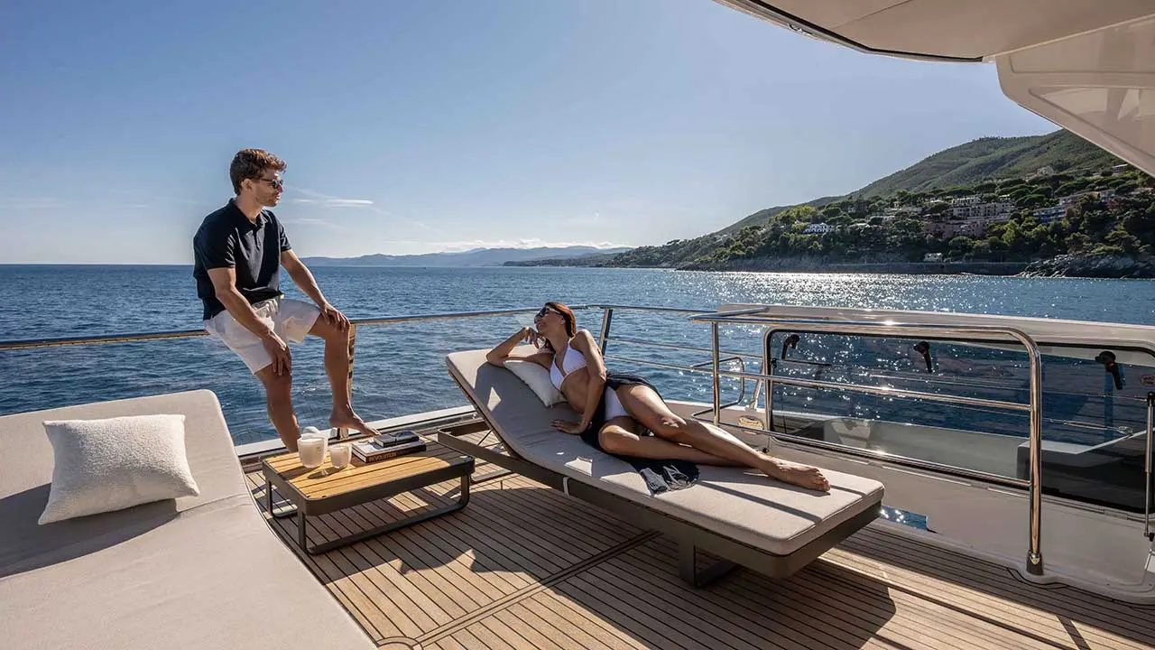 Couple relaxing on a luxury yacht deck overlooking sparkling sea and green coastal hills.