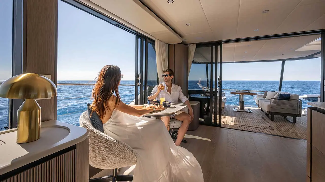 Couple dining in a luxury yacht saloon with panoramic windows overlooking the ocean.