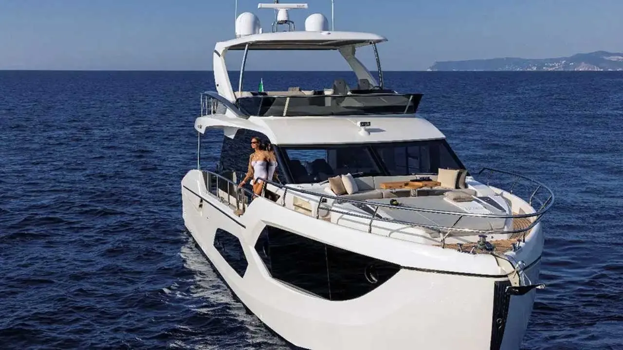 Luxury white motor yacht with a woman on deck, cruising across the sea with a distant coastline in the background.