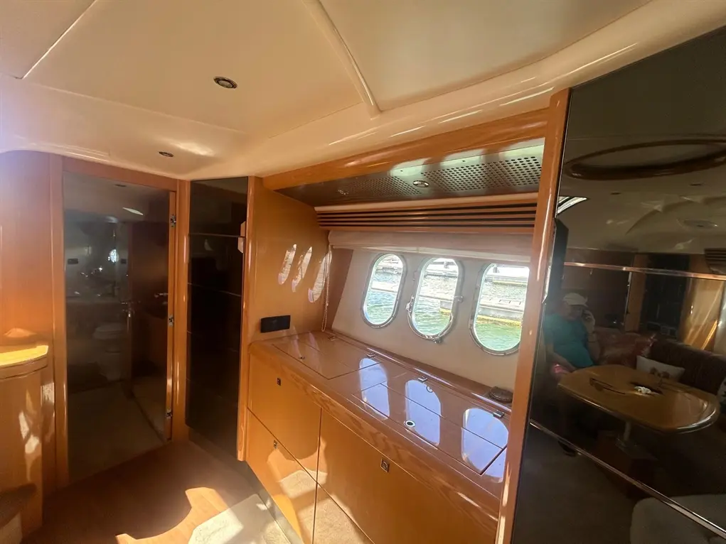 Interior of a yacht featuring wooden cabinetry, large oval windows, and a person sitting in a lounge area.
