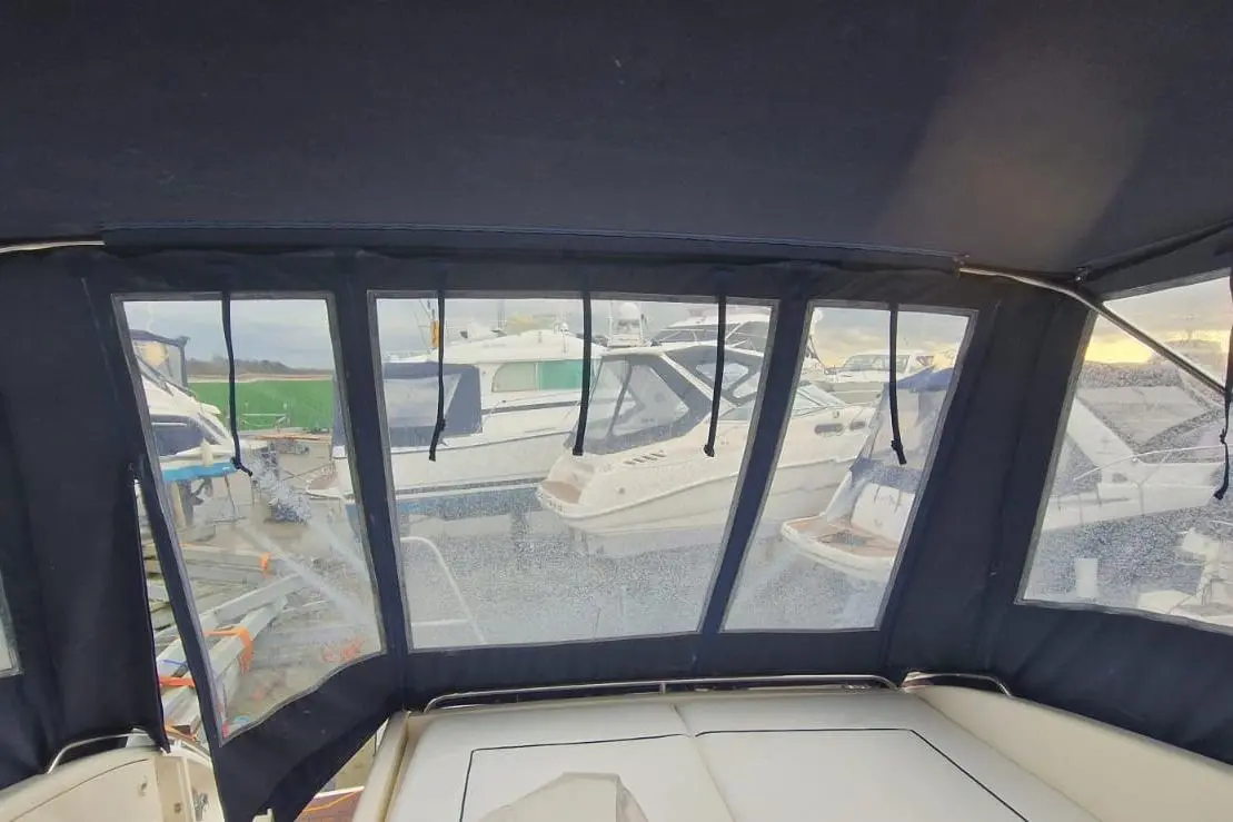 View from inside a boat cabin showing clear windows, with several other boats visible at a marina.