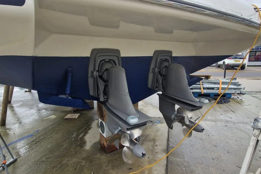 Two outboard motors mounted on the stern of a boat, with visible propellers resting on a concrete surface.