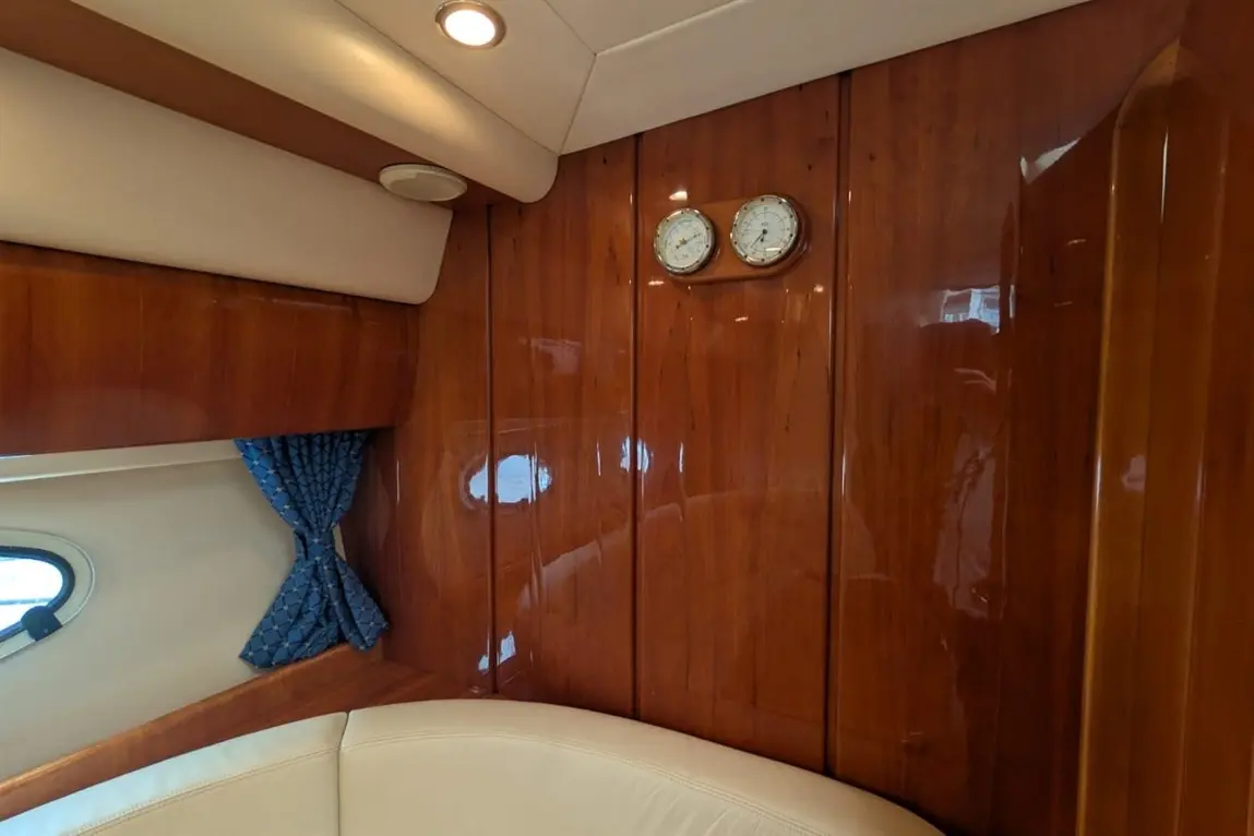 Interior of a yacht featuring polished wooden paneling, a white leather seat, a blue curtain, and two decorative clocks.