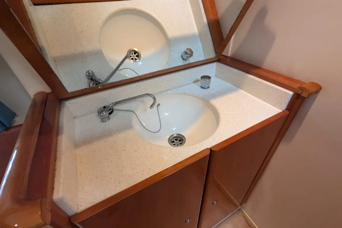 A modern bathroom washbasin with a chrome tap, white basin, wooden cabinetry, and a mirrored backsplash.